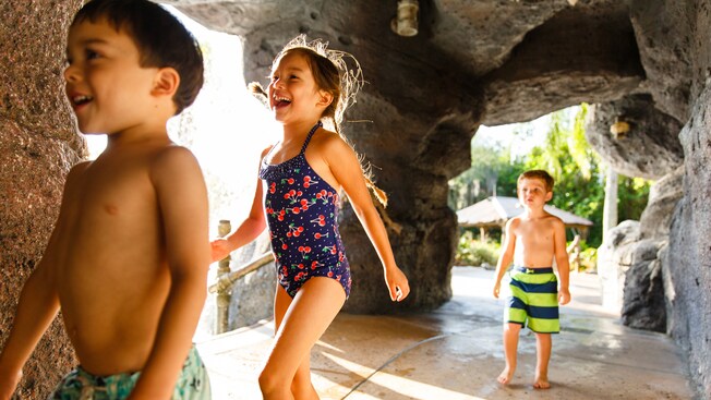 Three kids in swimsuits walking though a cave-like structure at Ketchakiddee Creek