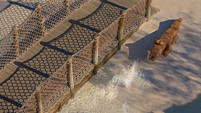 A wooden foot-bridge next to a crocodile and a small geyser-like fountain
