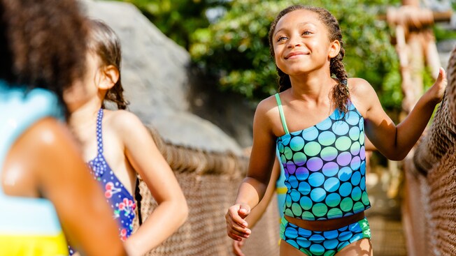 A girl in a swimsuit smiles as she cross a wooden foot-bridge