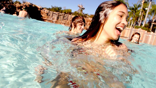 A teenage girl and 2 friends smile while standing in Disney's Typhoon Lagoon Surf Pool 