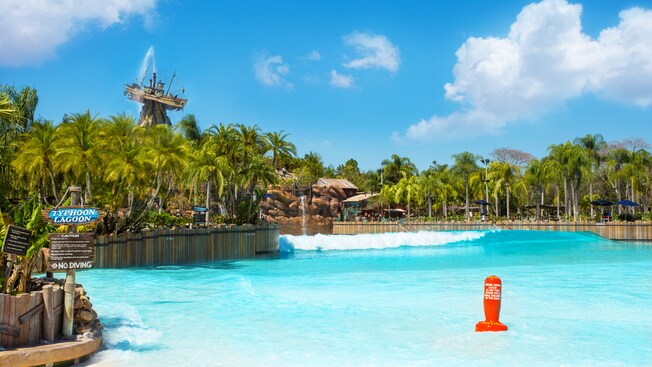 A large wave breaks in Disney's Typhoon Lagoon Surf Pool, with Mount Mayday in the background