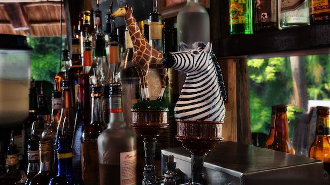Two beer tab-levers, with a zebra and a giraffe handle, next to liquor bottle at the back of the bar
