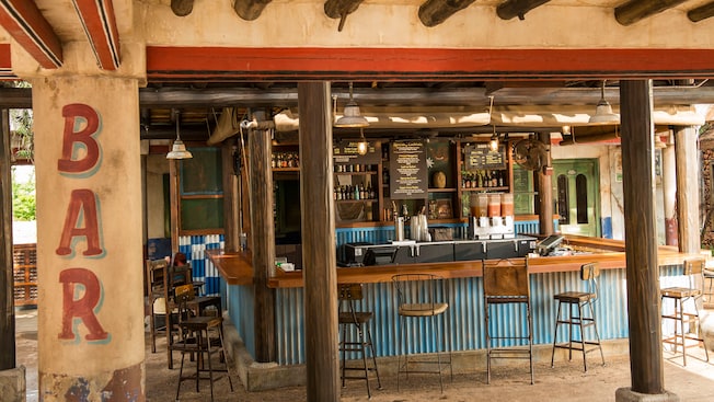 Wood pillars cascade from the ceiling as steel panels and stools line the counter at an outdoor bar