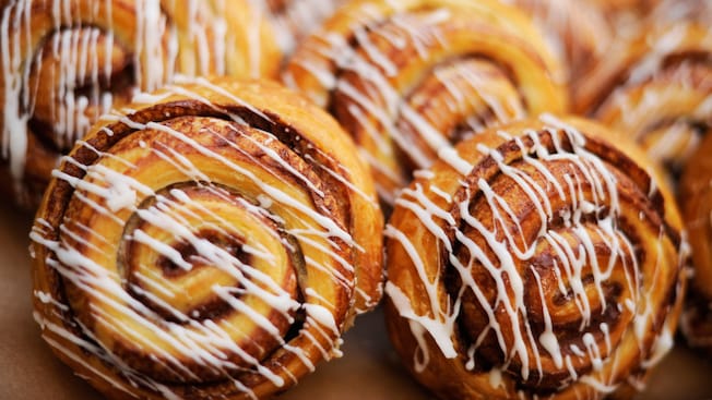Several cinnamon rolls, each with white drizzle glaze, standing on edge