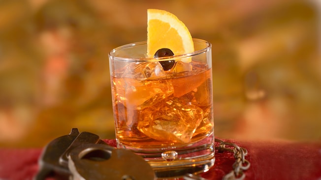 A specialty cocktail served in an Old Fashioned glass, garnished by a lemon slice and a black cherry