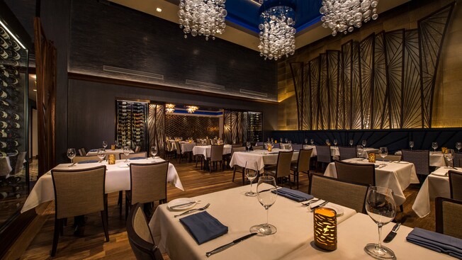 Large metal wall sculptures face rows of wine racks on opposing walls with dining tables in between