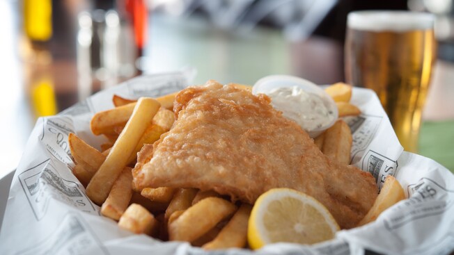 Basket of fish and chips with tartar sauce and lemon, with pint of beer in background