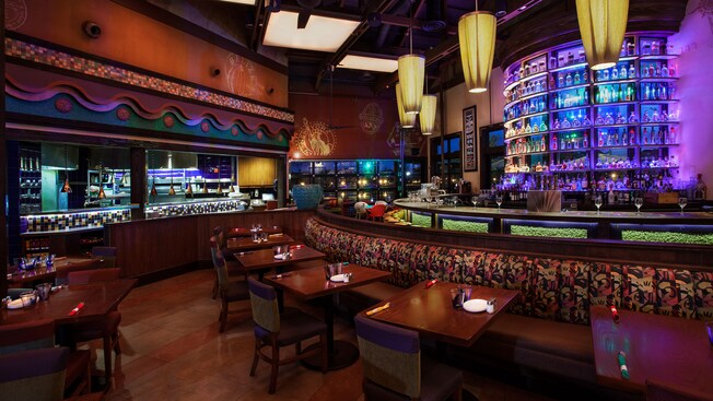Banquette tables in front of semicircular bar and lit tequila display, across from an open kitchen