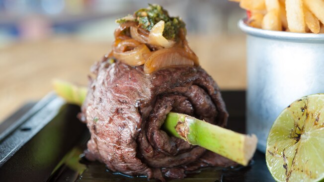 Argentinean skirt steak topped with onions and rolled around a bamboo stick, with fries in a cup