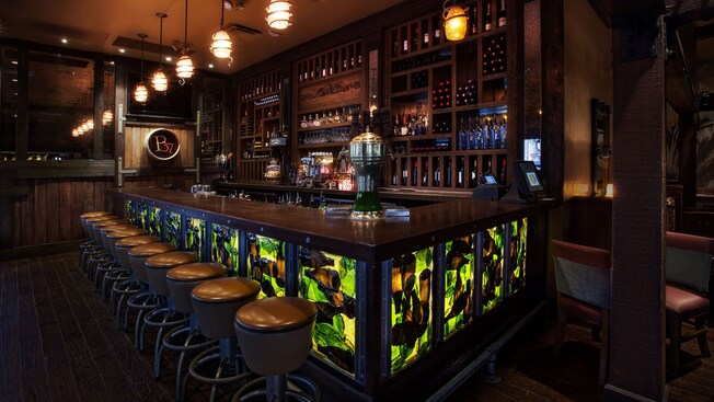 Upstairs wine bar with round padded stools, rustic wooden floors, paneling and wine racks 