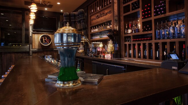 Beer taps sit on the corner of a wooden bar, with bottles of wine and liquor displayed on shelves 