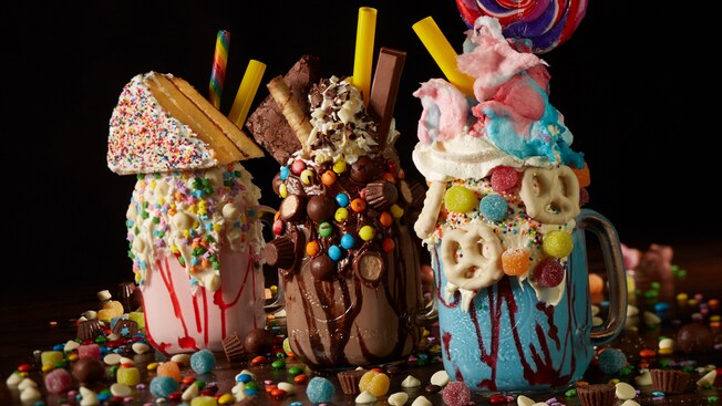 3 batidos grandes cubiertos con una variedad de dulces, un pastel, galletas y pretzels