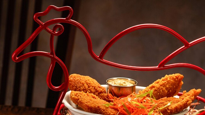 Una canasta con forma de gallina llena con dedos de pollo fritos, servidos con una cerveza