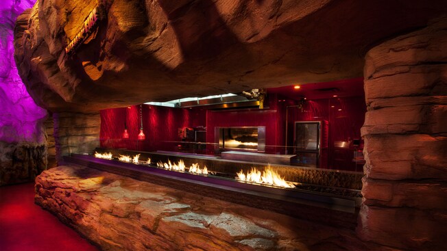 Una pared de piedra que enmarca una cocina abierta y parrilla con llamas