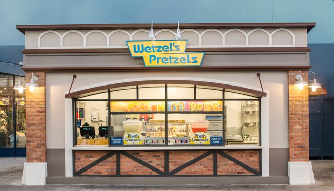 An outdoor quick-service restaurant with 2 windows and a sign that reads ‘Wetzel’s Pretzels’