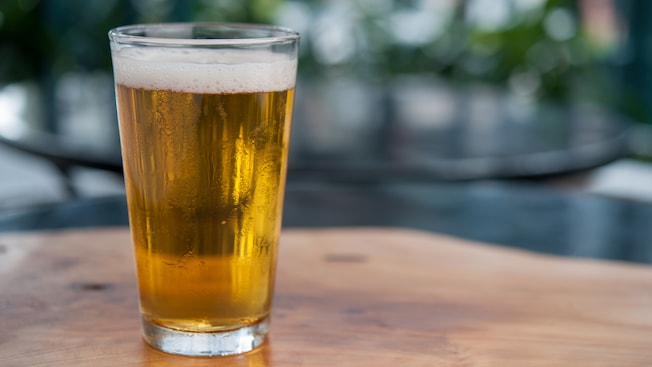 A plastic cup filled with frosty, frothy ale, served atop a wooden outdoor table