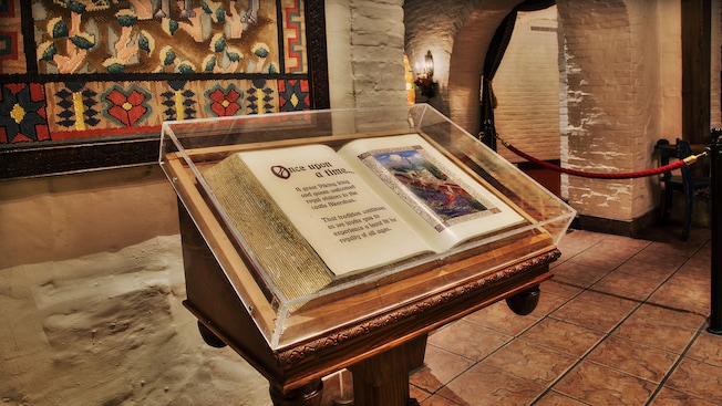 An open storybook with gold-leaf pages inside a Plexiglas case on a podium