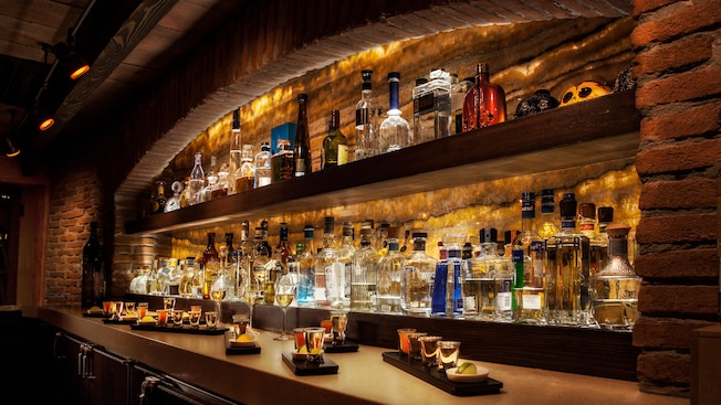 Shelves holding bottles of liquor with small trays holding shot glasses of tequila