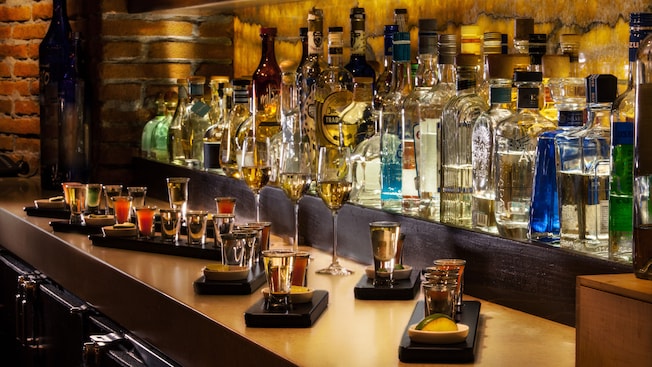 Close-up of a shelf holding bottles of liquor with small trays holding shot glasses of tequila