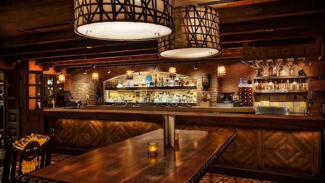 Dining table and chair, overhead lights and bar in the background