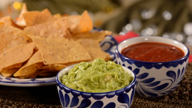 A plate of tortilla chips next to a bowl of guacamole and a bowl of salsa