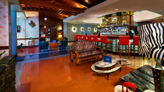 Colorful seating area next to the bar, with tables, patio furniture, chairs, a lamp and TV sets