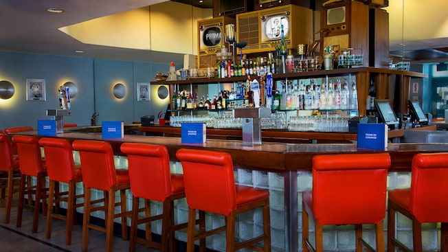 Stool-chairs at a wooden bar and an old TV above shelves with liquor bottles