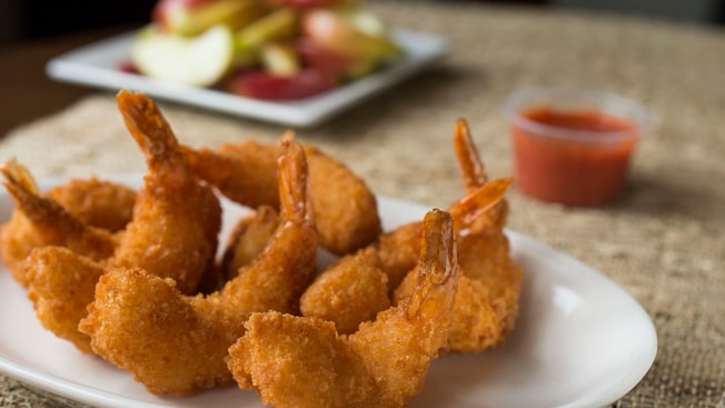 A platter of crispy fried shrimp, with apple slices and dipping sauce in the background