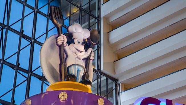 El chef Mickey en 3D con un tenedor y una cuchara gigante sobre el letrero de Chef Mickey's