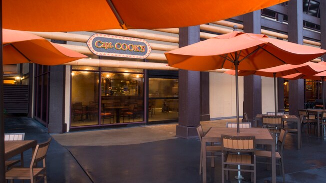 Exterior of restaurant with outdoor tables, chairs and umbrellas and a sign that says ‘Capt. Cook’s’