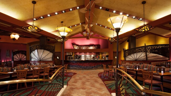 Pasillo iluminado por lámparas a la cocina abierta, bajo techo con vigas y ventiladores de ratán en movimiento