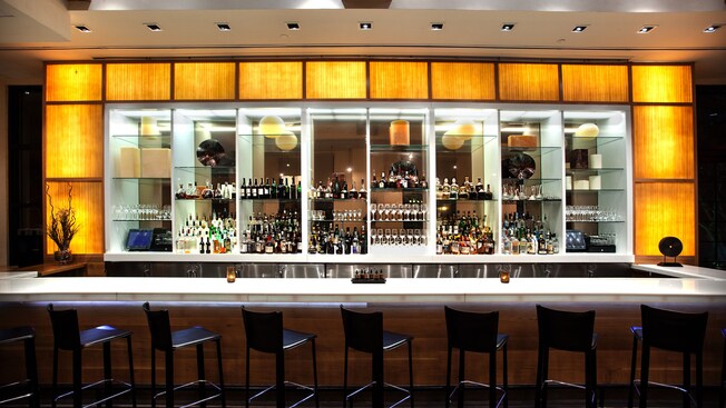 El bar Il Mulino Lounge y estantes llenos de vino y licor, con una fila de taburetes enfrente