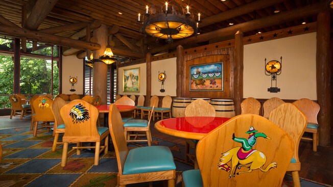 Parte del comedor se encuentra cerca de una pared con pinturas de vaqueros y un ventanal del piso al techo