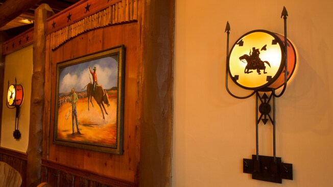 Pared del comedor con candelabros de diseño vaquero y una pintura de un rodeo