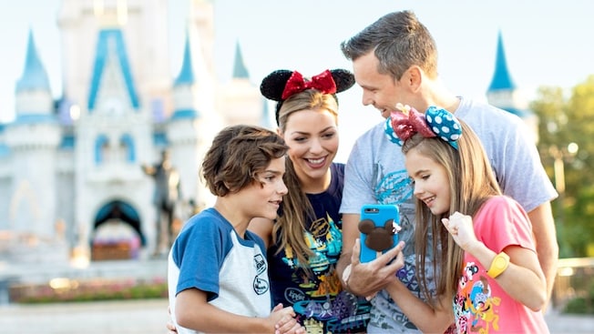 A family looks at a cellphone with a Disney cover in front of Cinderella Castle