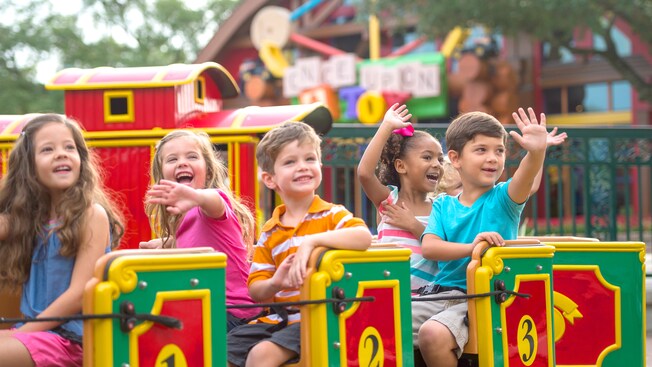 A half dozen young boys and girls smile and wave as they ride the Marketplace Train at Disney Springs