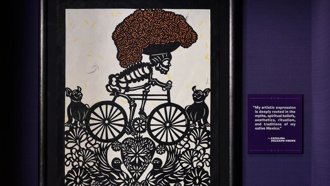 Pintura de un esqueleto en bicicleta cerca de dos perros