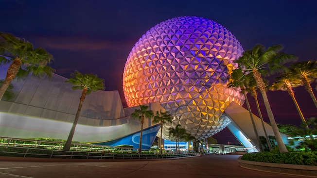 Evening lights casting a colorful glow onto Spaceship Earth as it rises into the sky above Epcot