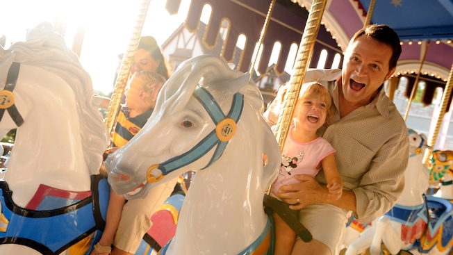 A dad holds his young daughter while riding a horse on Prince Charming Regal Carrousel