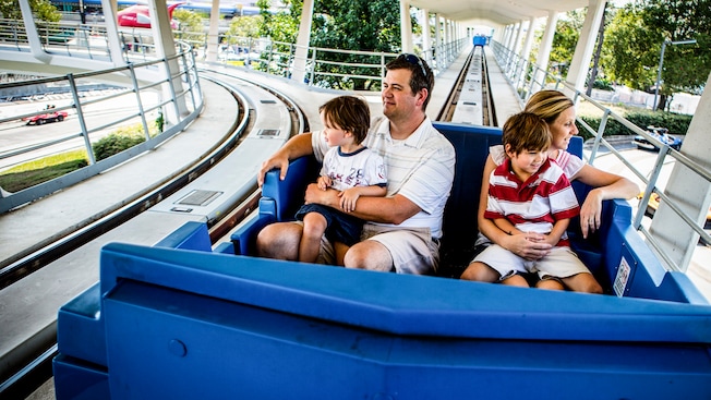 A mom and dad, each holding a young son, ride Tomorrowland Transit Authority PeopleMover