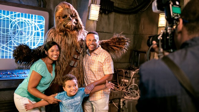 A mother, father and young son smiling while they pose alongside Chewbacca at ‘Star Wars’ Launch Bay