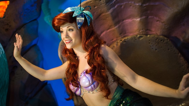 Ariel smiles and waves in an aquatic cave