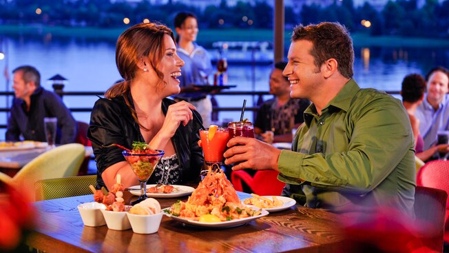 A woman and man share a laugh as they toast over their dinner