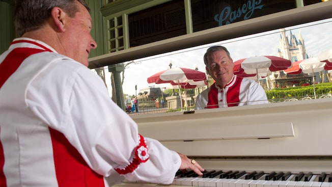 A piano player plays a piano at Casey's Corner with Cinderella's Castle reflected in a mirror