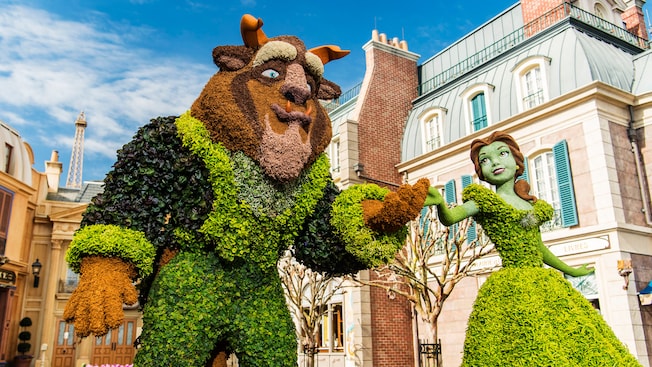 Topiaries of Belle and the Beast near stone buildings