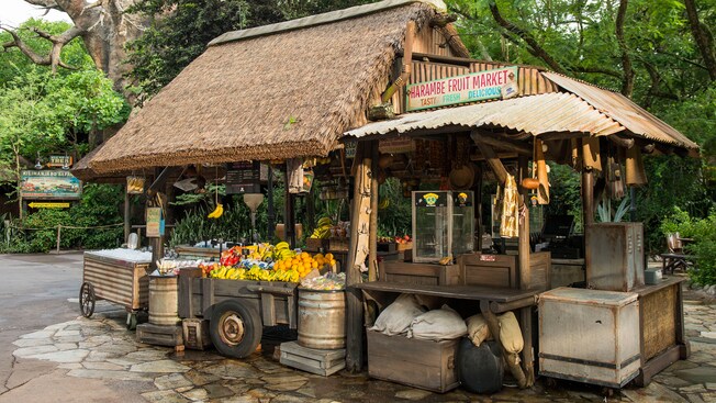 A rustic kiosk called Harambe Fruit Market displaying fresh fruit, bags of chips and assorted snacks