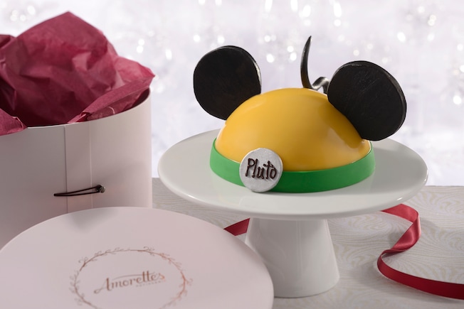 An Amorette’s Patisserie Pluto dome cake on a pedestal next to its hat box packaging