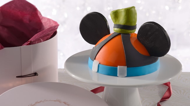 A dome cake decorated like Goofy next to a box that says ‘Amorette’s Patisserie’