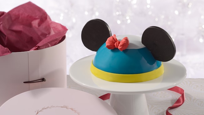 An Amorette’s Patisserie Donald Duck dome cake on a pedestal next to its hat box packaging