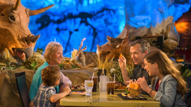 A girl and her dad enjoy waffle fries seated at their table with Dinosaur themed decor in the background